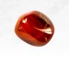 A vibrant image of a carnelian crystal chunk, featuring warm hues of orange, red, and brown. The crystal's smooth surface and rich coloration evoke a sense of passion, creativity, and motivation.