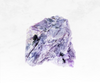A captivating image of a charoite crystal chunk, showcasing a deep purple color with streaks of white, black, and lavender. The crystal's swirling patterns and unique markings evoke a sense of transformation, spiritual growth, and inner exploration.