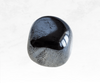 A striking image of a hematite crystal chunk, featuring a metallic gray-black color with a polished and reflective surface. The crystal's smooth texture and solid presence evoke a sense of grounding and protection, symbolizing strength and resilience.