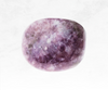 A photograph showcasing a lepidolite crystal chunk, characterized by its soft lilac to purple color and mica-like sparkle. The stone's gentle energy promotes relaxation and inner peace.