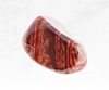 An image of a red jasper crystal chunk, displaying deep red tones with subtle variations and earthy patterns. The stone's grounding energy fosters strength, stability, and vitality.